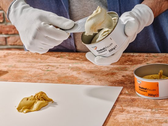 Witte handschoenen nemen een spatel met romige, crèmekleurige houtrotvuller uit een blik "Houtrotvuller Component A 250G".