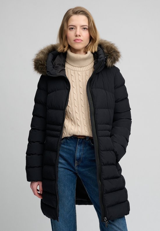 Lange zwarte pufferjas met bontkraag, gedragen door een blond model met beige coltrui en spijkerbroek.