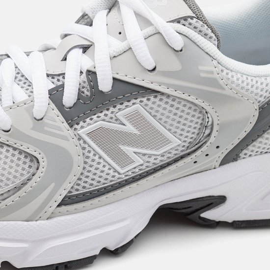 Grijze sneaker met witte veters en een zilverkleurig 'N' logo op de zijkant.