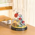 Glazen stolp met micro mini blokjes: bloemen, lieveheersbeestjes en een teddybeer. De stolp staat op een houten tafel.