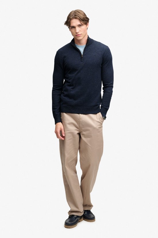 Man met donkerblauwe melange trui met ritssluiting, lichtblauw T-shirt en beige broek.