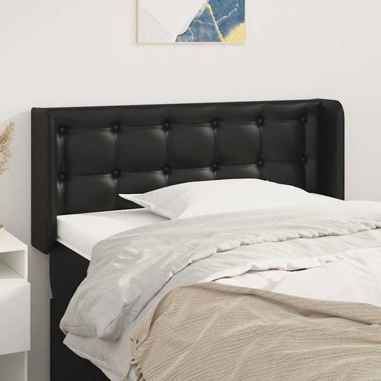 Tête de lit noire à boutons, sur un lit avec draps blancs.