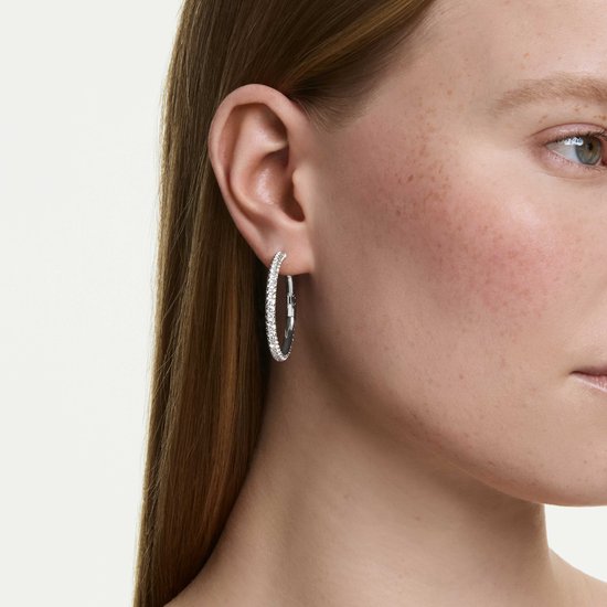 Model draagt zilverkleurige creolen bezet met witte kristallen.
