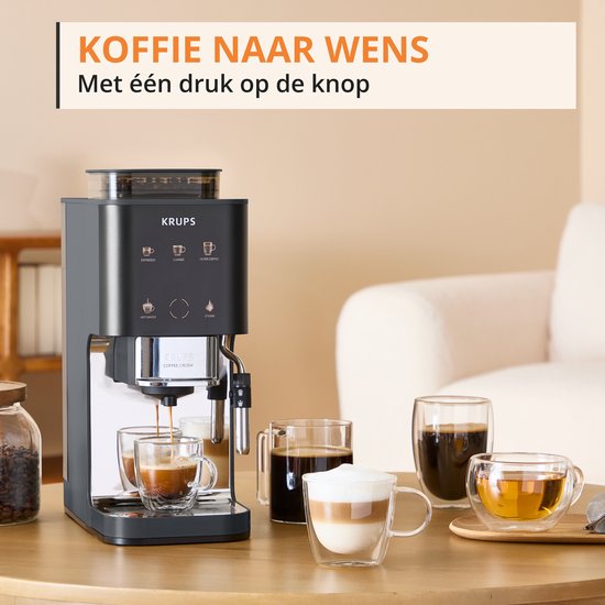 Grijze Krups volautomatische espressomachine op tafel, met glazen mokken koffie en thee.