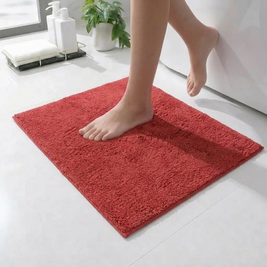 Een rood, vierkant badmatje met een pluizige textuur, waarop een persoon uit een bad stapt.