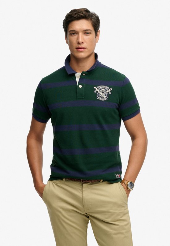 Man staand, draagt een donkergroene polo met marineblauwe strepen, geborduurd logo.