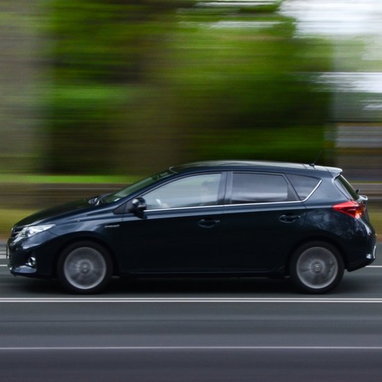 Een donkerblauwe hatchback rijdt op een weg, de achtergrond is wazig groen.
