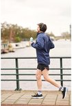 Homme en veste bleu marine, short de sport noir et chaussettes blanches à rayures, faisant du jogging avec une bouteille.