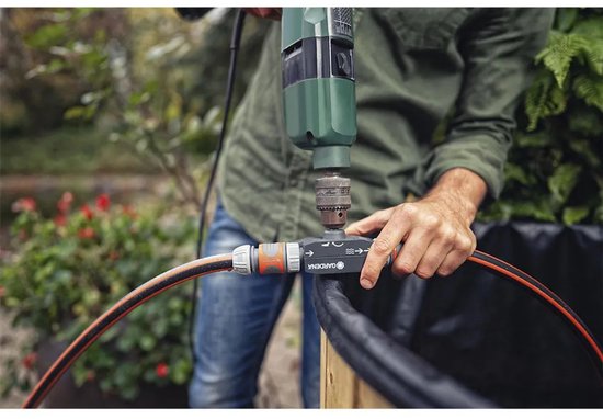 Close-up van een man die een Gardena voorzetpomp met boormachine op een tuinslang bevestigt.