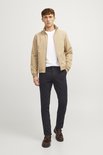 Man met beige bomberjack, wit T-shirt en zwarte chino.
