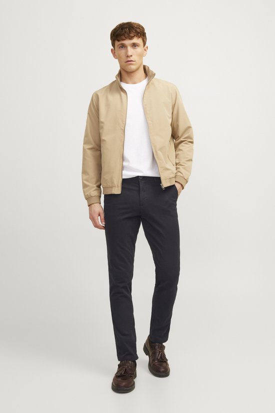 Man met beige bomberjack, wit T-shirt en zwarte chino.