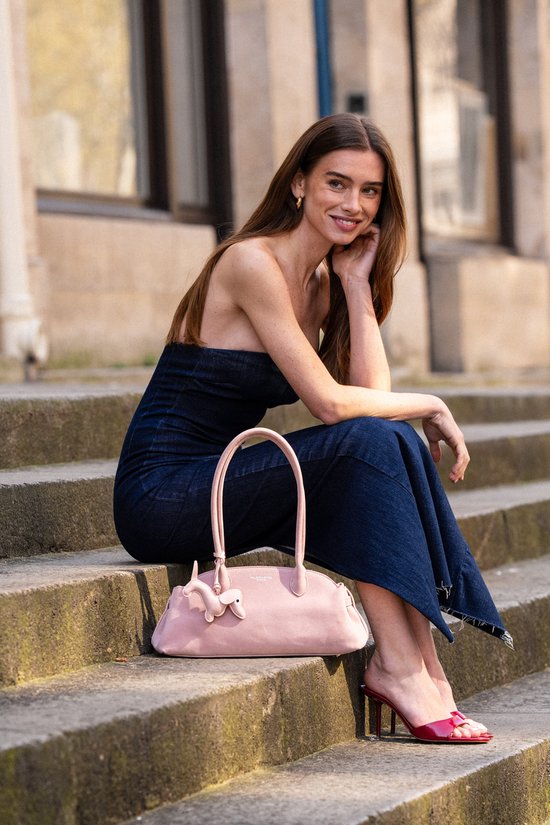 Model met een lichtroze handtas met teckel versiering op een trap.