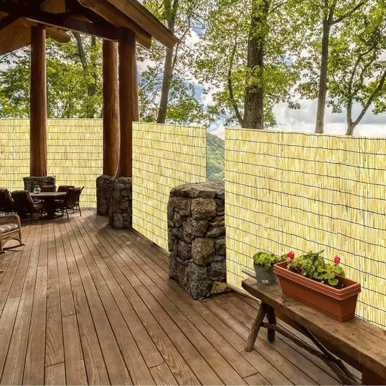 Rieten privacyscherm rondom een houten terras met tuinmeubilair en plantenbakken.