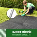 Man slaat een grondpin in een zwarte onkruiddoek met behulp van een hamer. Gedetailleerde weergave van de pin.