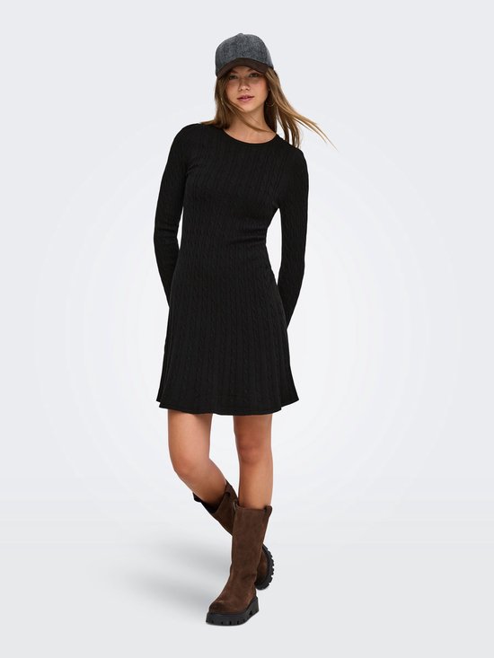 Model in een zwarte gebreide mini-jurk met kabels, lange mouwen, bruine laarzen en een pet.