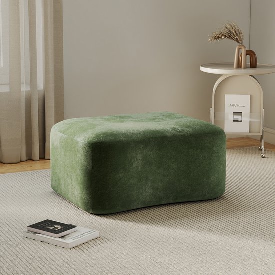 Groen, fluwelen voetenbankje in een woonkamer, met een bijzettafel en een boek op de grond.