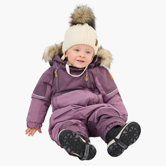 Zittend kind in paarse winteroverall met capuchon, imitatiebont, crème muts en zwarte laarzen.