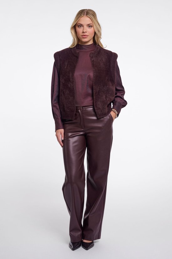 Model van voren in donkerbruine wollen gilet, blouse met lange mouwen en wijde leren broek.