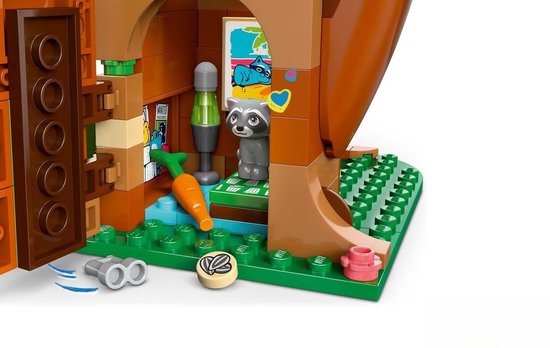 Grijze LEGO-wasbeer en staande groene lamp naast een LEGO-wortel in een bruine boomhut met posters en een blauw hart.