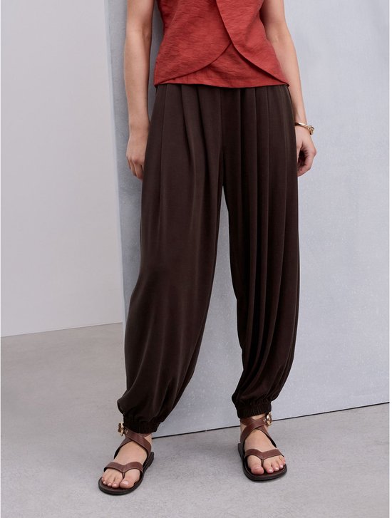 Model draagt een bruine ballonbroek met een roodbruine top en bruine sandalen.
