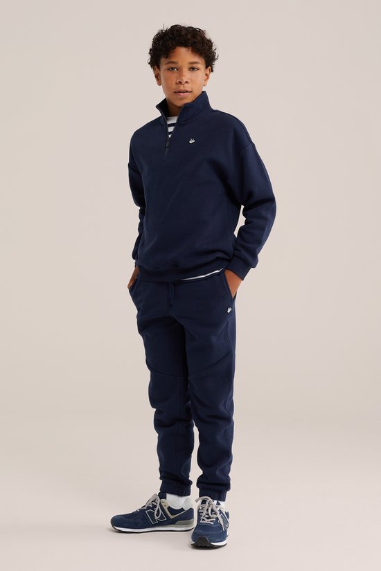 Jongen in volledig donkerblauwe joggingpak, met hands in pockets.
