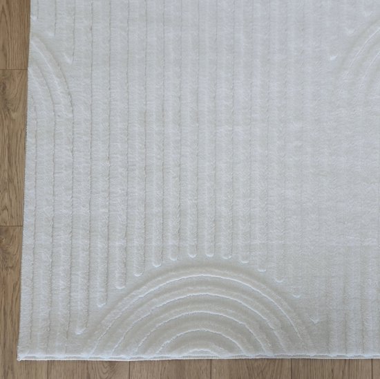 Crème laagpolig vloerkleed met een gebogen lijnpatroon en verticale ribbels, op een houten vloer.