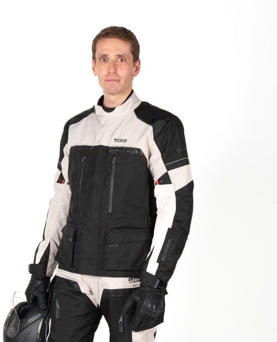 Man draagt een DXR motorjas in zwart en grijs, met rode accenten. Hij draagt handschoenen en houdt een helm vast.
