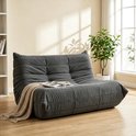 Grijze vloersofa met zachte stof en een deken, geplaatst in een woonkamer.