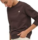 Model draagt bruine sweater met witte hart-applicatie, met de hand in de zak.