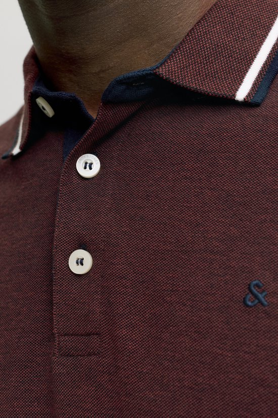 Close-up van bordeauxrode polo met twee witte knopen, geborduurd logo en gestreepte kraag.