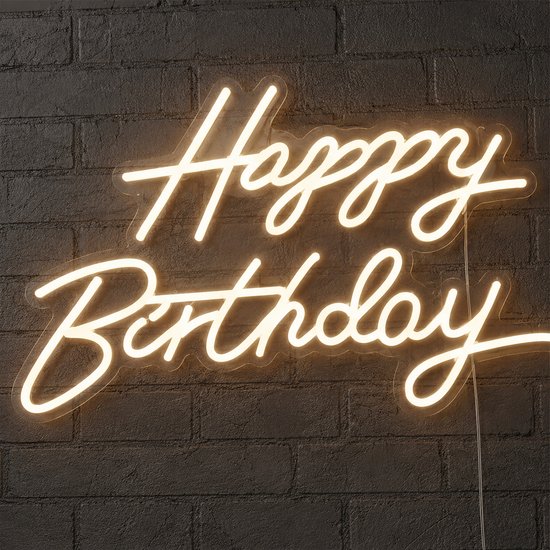 Een warmwit "Happy Birthday" neonbord op een donkere bakstenen muur.