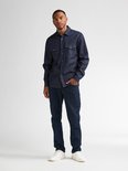 Man in donkerblauw denim overhemd met lange mouwen, twee borstzakken en jeans.