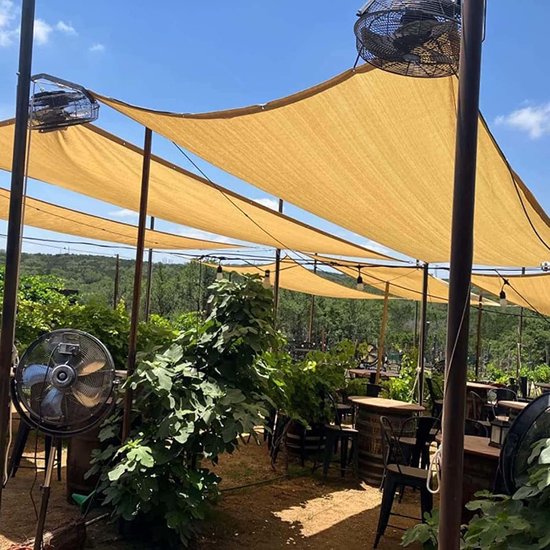 Tarieven beige schaduwdoeken over een buitenruimte met tafels, stoelen en planten.