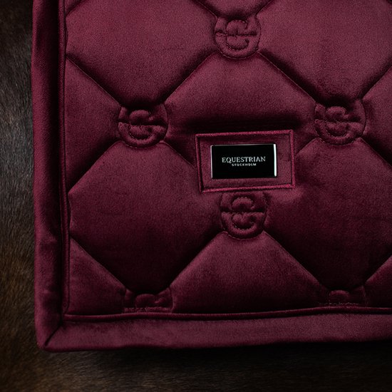 Donkerrode, gepofte dressuur deken met diamantpatroon en Equestrain Stockholm logo.