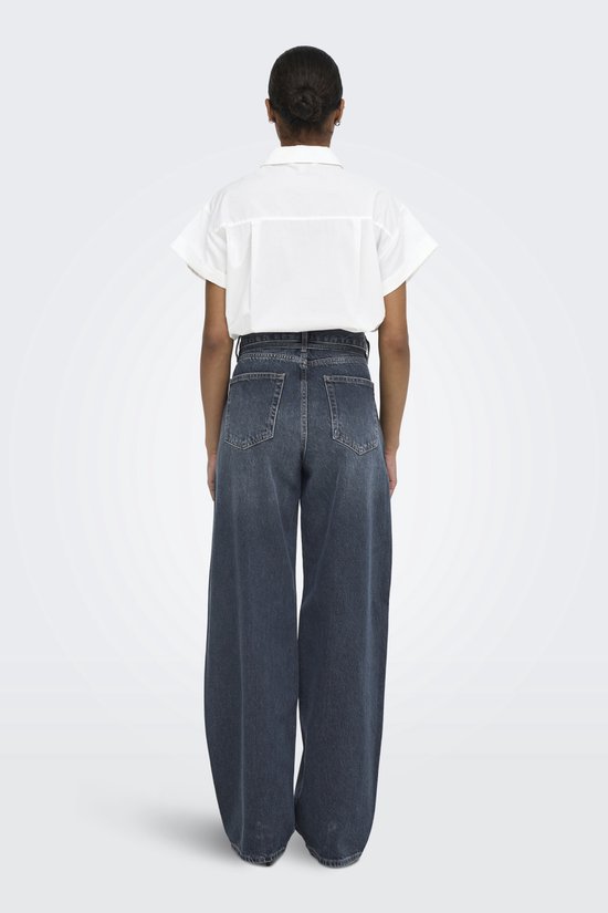 Model in wit shirt en donkerblauwe wijde jeans met strikceintuur, van achteren gezien.