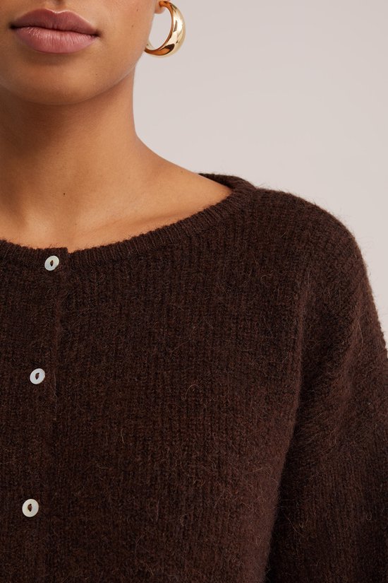 Detail van een bruin gebreid vest met witte knopen.