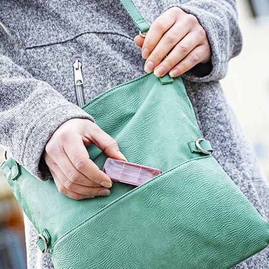 Une personne portant un manteau gris met une petite boîte à pilules rose dans un sac vert.