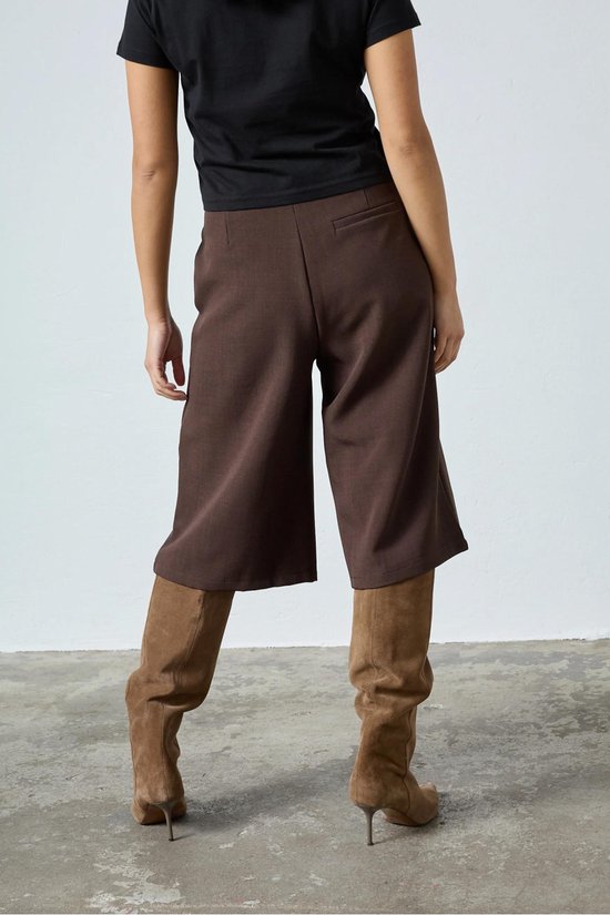 Model van achteren gezien in een bruine culottebroek met wijde pijpen en zwarte top.