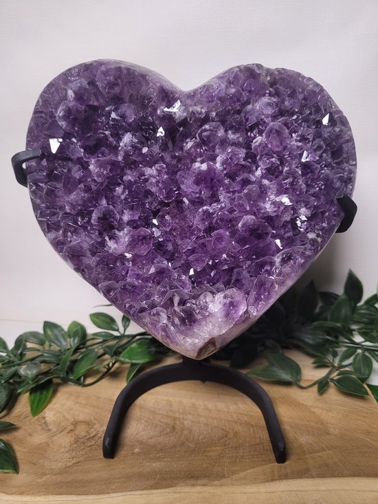 Hartvormige amethist geode met paarse kristallen op een standaard, omringd door groene planten.