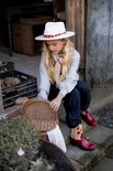 Meisje met witte hoed en rode cowboylaarzen met vlinderborduursel zit op een trap met een rieten mand.