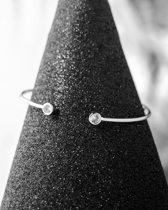Zilveren open armband met twee heldere ronde stenen, tentoongesteld op een glinsterende zwarte kegel.