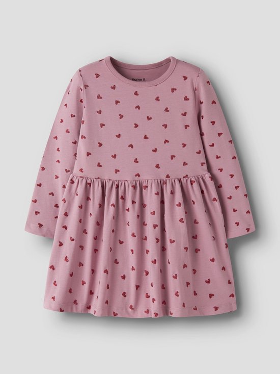 Lichtroze jurk met lange mouwen en een all-over print van rode hartjes. De jurk heeft een ronde hals en een ingesnoerde taille met een zwierige rok.