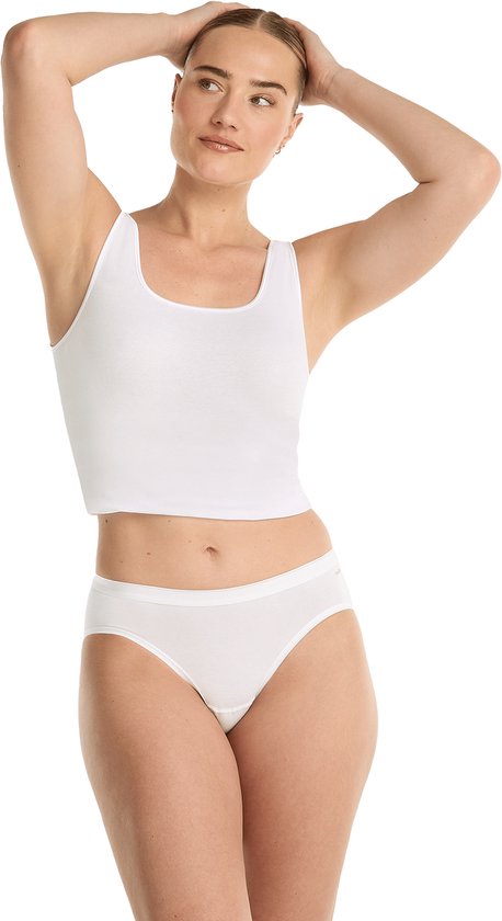 Vrouw in witte crop top en witte bikinislip, met handen achter het hoofd. Strakke pasvorm.