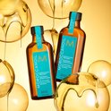 Twee flessen Moroccanoil Treatment in een gouden vloeistof-omgeving.