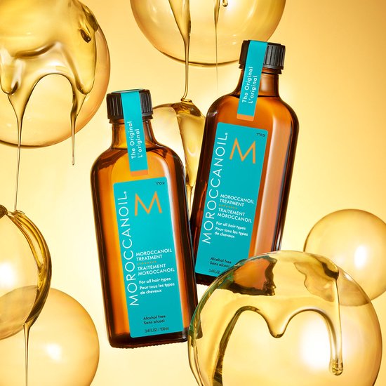 Twee flessen Moroccanoil Treatment in een gouden vloeistof-omgeving.