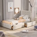 Beige gestoffeerd eenpersoonsbed met hoofdbord, 2 opberglades, een plaid en kussens. Een gestreept vloerkleed ligt ervoor.