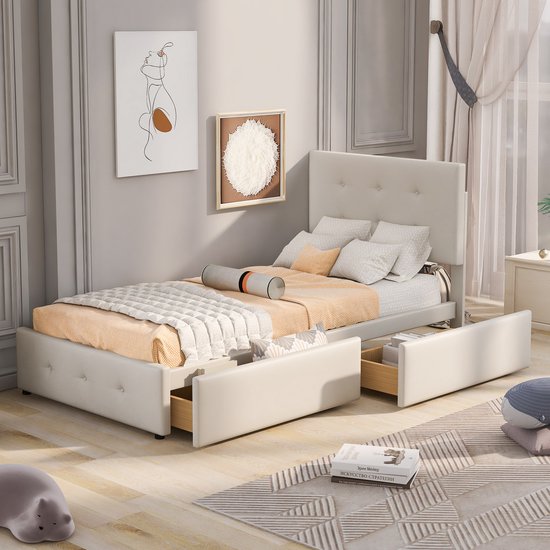 Beige gestoffeerd eenpersoonsbed met hoofdbord, 2 opberglades, een plaid en kussens. Een gestreept vloerkleed ligt ervoor.