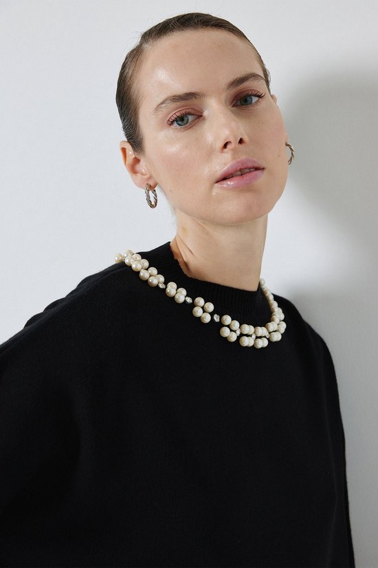 Model in zwart gebreid kledingstuk met een dubbele parelketting.