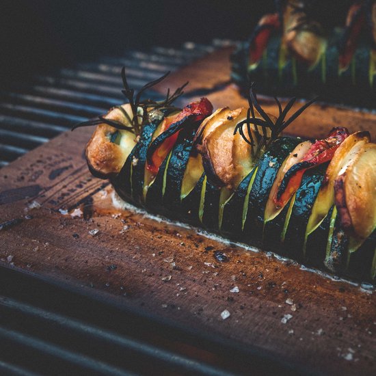Gegrilde courgette met tomaat, ui en rozemarijn op een houten plank.