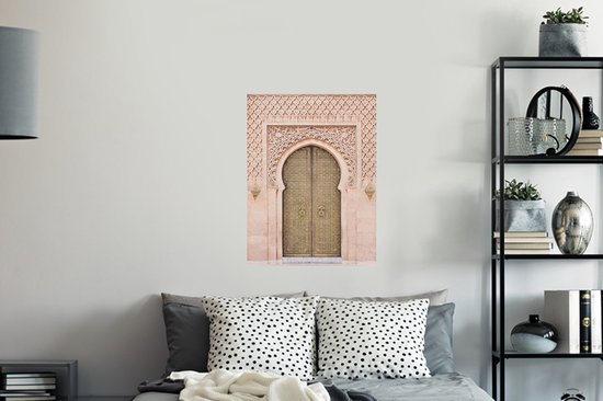 Une porte marocaine couleur sable avec des détails dorés et une sculpture sur pierre complexe, accrochée au-dessus d'un lit avec des oreillers à pois.
